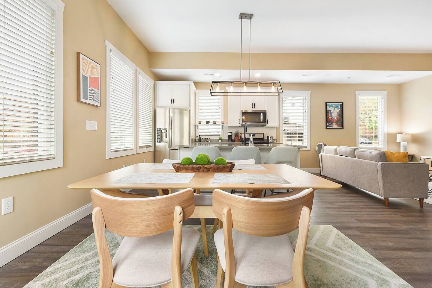 Una cocina moderna con armarios blancos, una isla central y un comedor con mesa y sillas de madera.