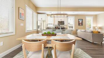 Una cocina moderna con armarios blancos, una isla central y un comedor con mesa y sillas de madera.