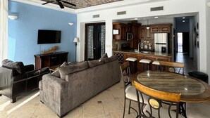 A spacious living area with a high ceiling featuring exposed brickwork, a grey sofa, a dining table with chairs, and a kitchen in the background. - Palacio Del Mar 102 - Rocky Point Oceanfront Vacation Rental (Puerto Peñasco)