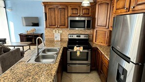 A kitchen with granite countertops, stainless steel appliances, wooden cabinets, and a pendant light. - Palacio Del Mar 102 - Rocky Point Oceanfront Vacation Rental (Puerto Peñasco)