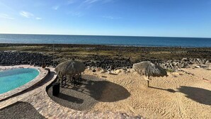 Un espace piscine situé au bord de la plage, offrant une vue dégagée sur l’océan et un rivage rocheux.