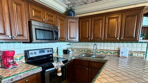 A kitchen with wooden cabinets, a stainless steel microwave, a stove, and a tiled backsplash. - Palacio Del Mar 307 - Rocky Point Oceanfront Vacation Rental (Puerto Peñasco)