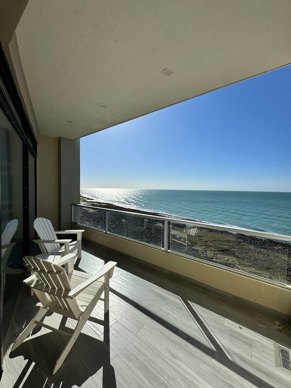 Ein Balkon mit Blick auf das Meer, ausgestattet mit einem Geländer und einigen Adirondack-Stühlen.