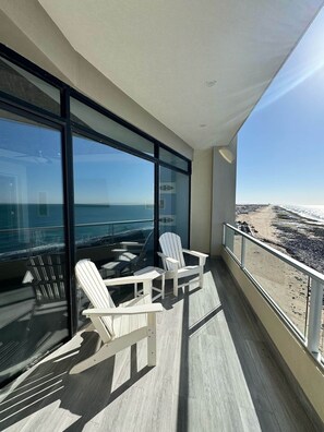 Un balcón con dos sillas Adirondack, un ventanal y vista a la playa y el océano.