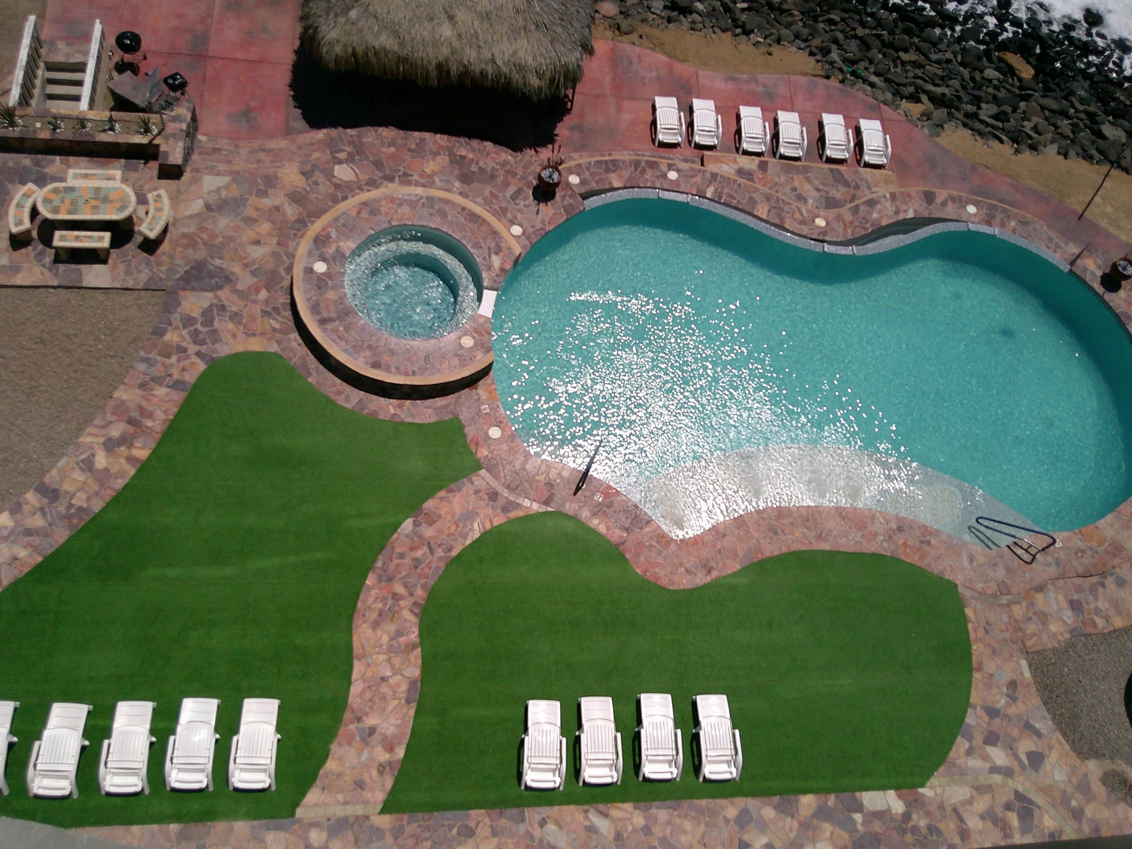A swimming pool with lounge chairs, a hot tub, and a stone-tiled deck.