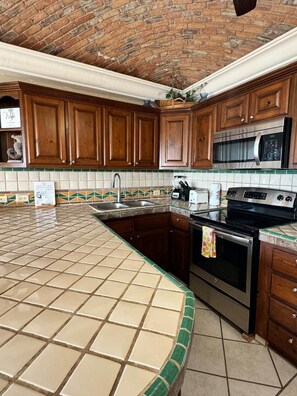 A kitchen with wooden cabinets, a microwave, an oven, and a tiled backsplash. - Palacio Del Mar 206 - Rocky Point Oceanfront Vacation Rental (Puerto Peñasco)