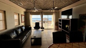 A living room with a brick ceiling, a black leather sofa, a coffee table, and a TV on a wooden stand. - Palacio Del Mar 106 - Rocky Point Oceanfront Vacation Rental (Puerto Peñasco)