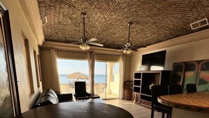 A spacious room with a brick ceiling, a round dining table, and a view of the beach. - Palacio Del Mar 106 - Rocky Point Oceanfront Vacation Rental (Puerto Peñasco)