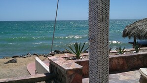 A beachside patio with a stone column, a thatched umbrella, and a metal showerhead. - Palacio Del Mar 106 - Rocky Point Oceanfront Vacation Rental (Puerto Peñasco)