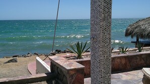 A beachside patio with a metal shower, a thatched umbrella, and a stone planter. - Palacio Del Mar 505- Rocky Point Oceanfront 4 Bedroom/4 Bath (Puerto Peñasco)