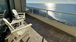 Un balcon avec deux chaises blanches, un plancher en bois et une vue sur l’océan.