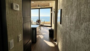 Un couloir étroit, avec de grandes fenêtres donnant sur l’océan, mène à un coin repas équipé d’une table et de chaises.