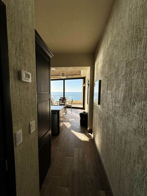 Ein schmaler Flur mit Blick auf das Meer durch große Fenster, der zu einem Essbereich mit Tisch und Stühlen führt.