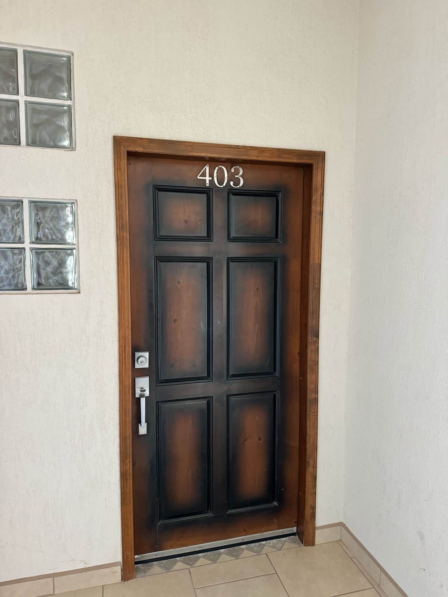 Uma porta de madeira escura com o número 403, uma fechadura digital e um interfone.