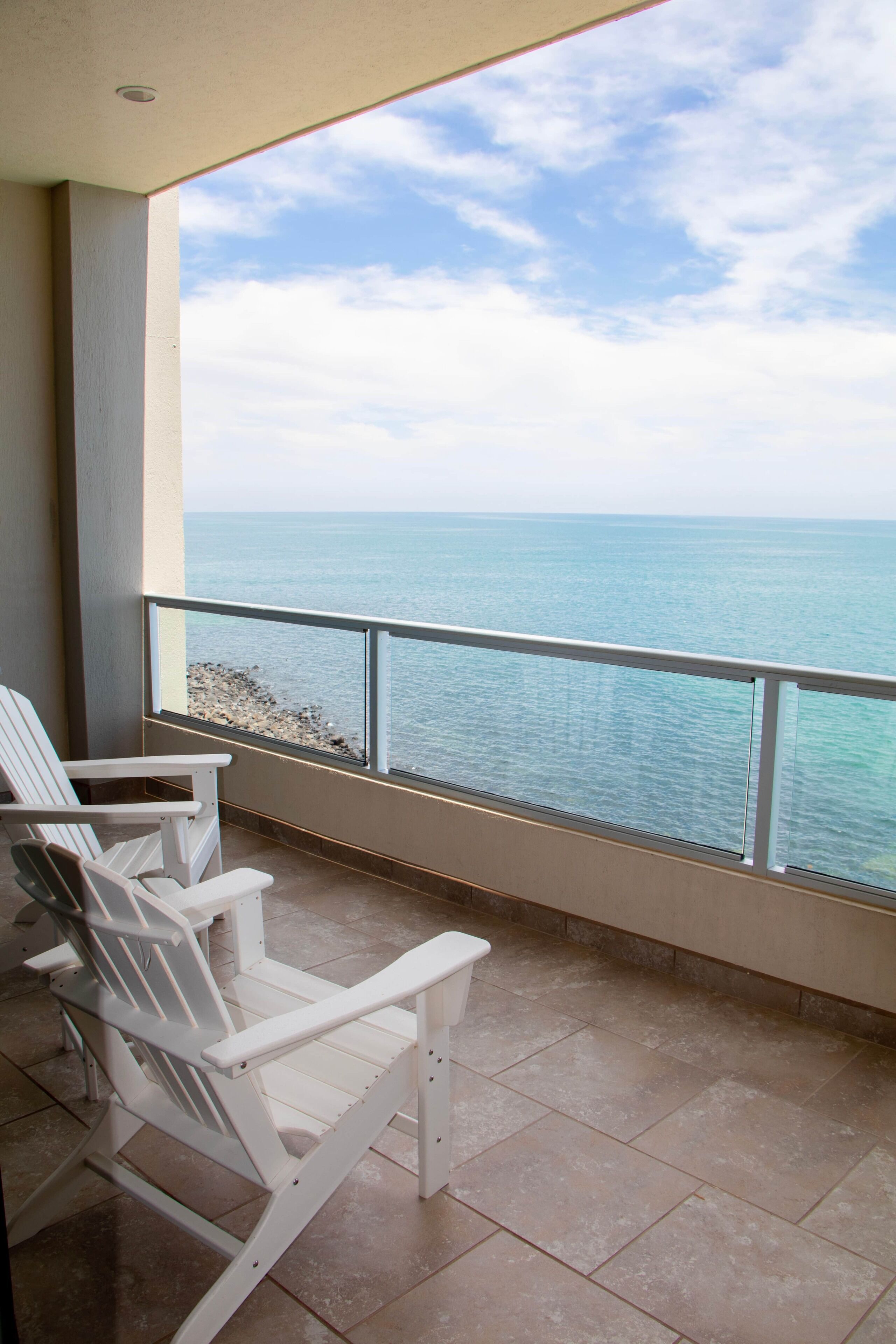 Ein Balkon mit zwei weißen Adirondack-Stühlen, der Blick auf das Meer geht.