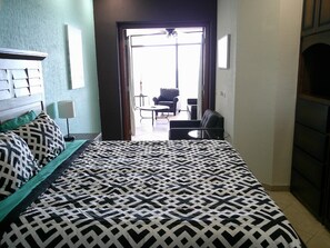 A hotel room with a bed, a nightstand, a lamp, and a view of the outside balcony. - Palacio Del Mar 201 - Rocky Point Oceanfront Vacation Rental (Puerto Peñasco)