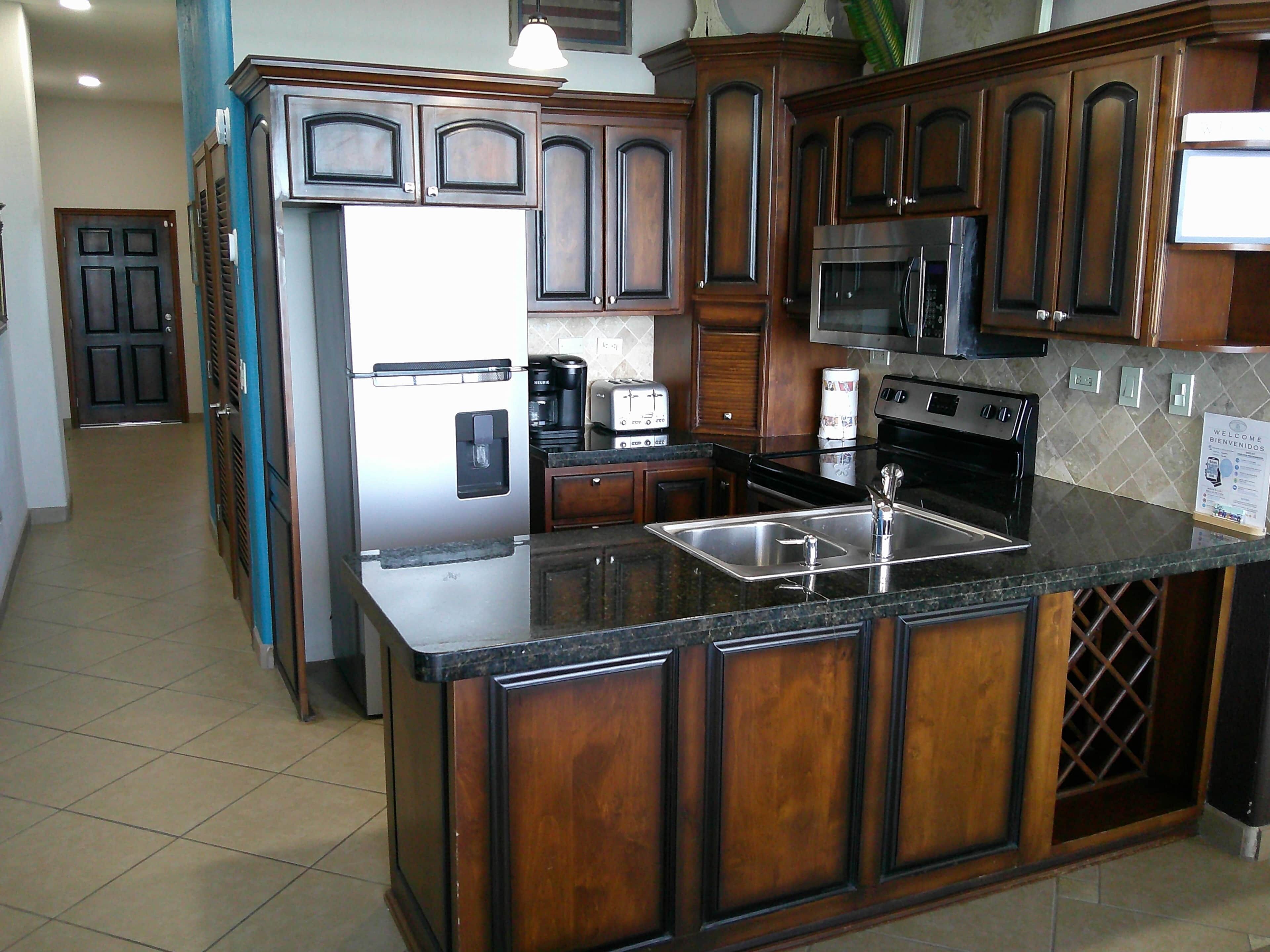 A kitchen with wooden cabinets, a stainless steel refrigerator, a microwave, a stove, and a sink.