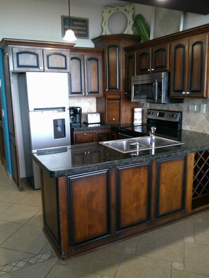 A kitchen with dark wooden cabinets, a stainless steel refrigerator, a microwave, and a stove. - Palacio Del Mar 201 - Rocky Point Oceanfront Vacation Rental (Puerto Peñasco)