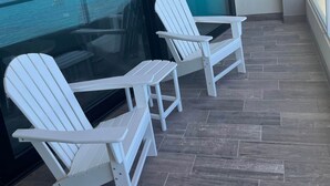 En balkon med to hvide Adirondack-stole, en glasdør og udsigt til havet.
