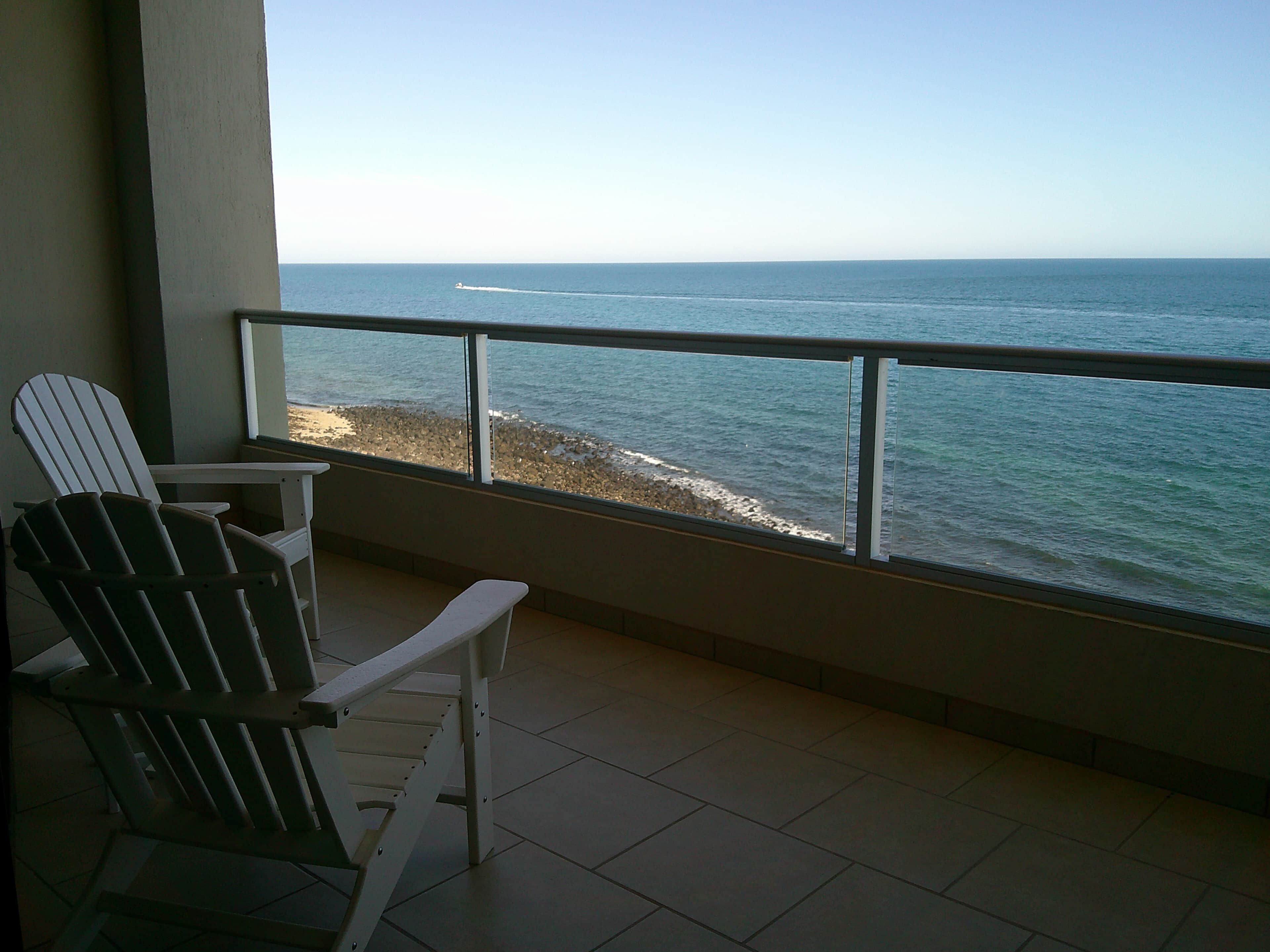 Ein Balkon mit zwei Adirondack-Stühlen, der auf eine felsige Küstenlinie und den Ozean blickt.