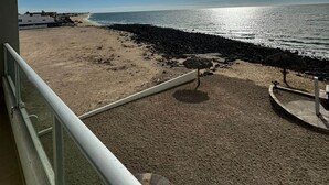 A beach view from a balcony with a railing, a thatched umbrella, and a rocky shoreline. - Palacio Del Mar 202 - Rocky Point Oceanfront Vacation Rental (Puerto Peñasco)