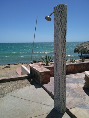 A beachside patio with a stone column, a thatched umbrella, and a metal showerhead. - Palacio Del Mar 202 - Rocky Point Oceanfront Vacation Rental (Puerto Peñasco)