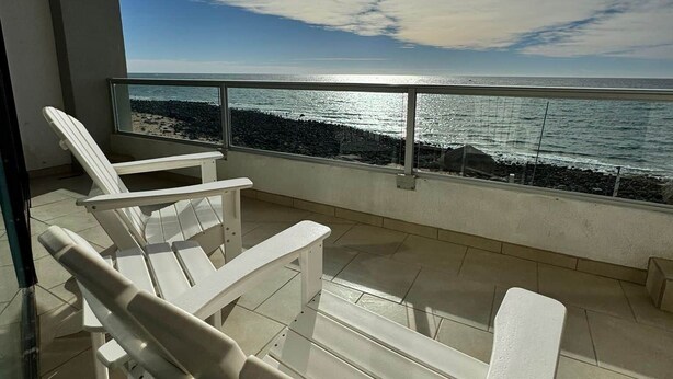 A balcony with white lounge chairs, a glass railing, and a view of the ocean. - Palacio Del Mar 202 - Rocky Point Oceanfront Vacation Rental (Puerto Peñasco)