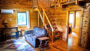 A log cabin interior with a wooden staircase, a leather couch, a small table, and a colorful rug. - Horseshoe Canyon Ranch (Jasper)