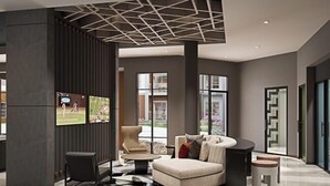 A modern interior with a sectional sofa, a round coffee table, and a patterned rug. There are large windows providing natural light and a view of the outdoors. - Landing Furnished Apartments West Huntsville (Huntsville)
