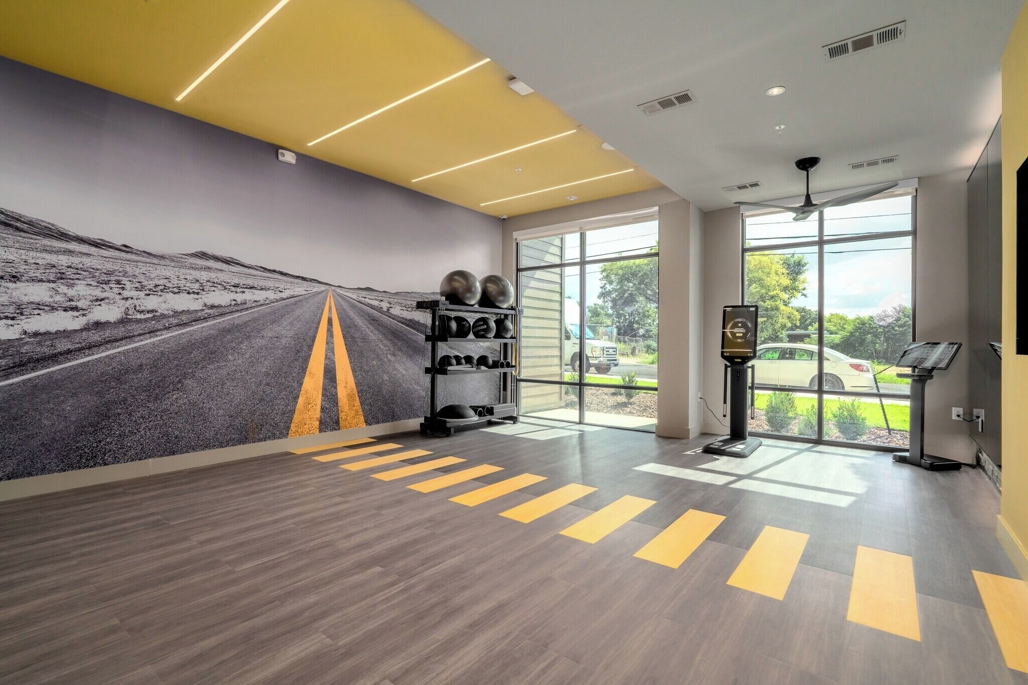 A gym with a road mural, exercise equipment, and large windows.