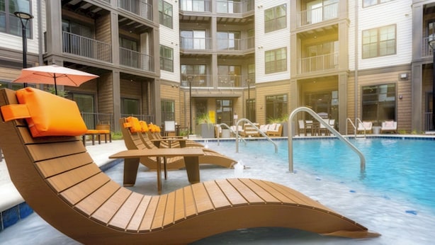 A pool area with sun loungers and a small table, surrounded by a multi-story building with balconies. - Landing Furnished Apartments West Huntsville (Huntsville)