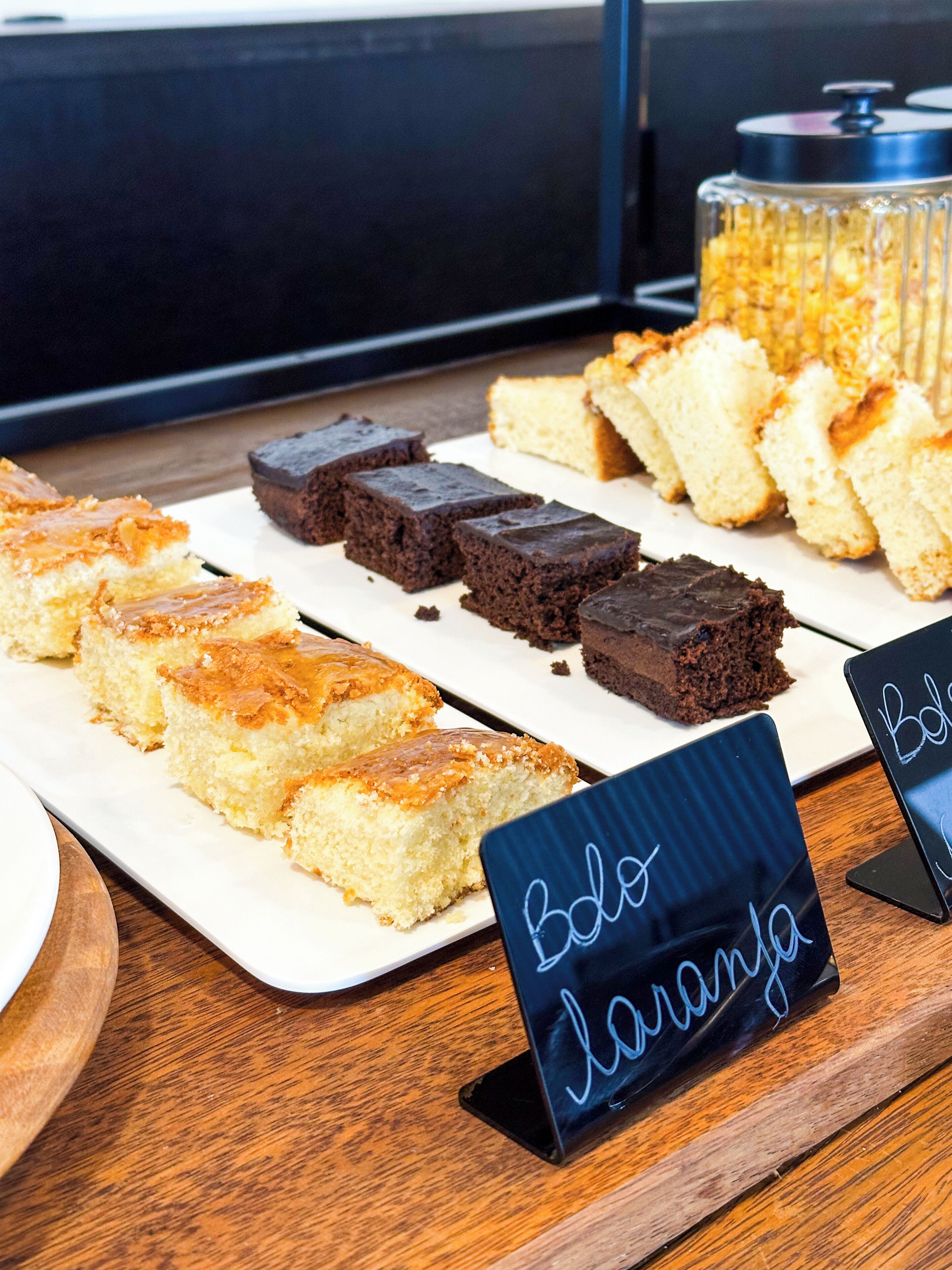 Una presentación de postres con varios pasteles y brownies, un letrero en una pizarra y un frasco al fondo.