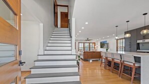 A modern kitchen with a central island, wooden bar stools, and pendant lighting. - 5 BR Canal front Retreat w/ Dock, EV Charger & 3-Min Walk to Holden Beach (Holden Beach)