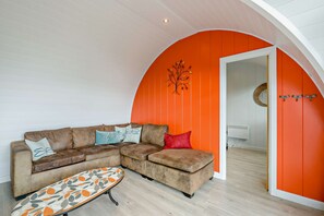 A cozy living area with a brown leather sofa, a patterned ottoman, and a vibrant orange accent wall. - Host & Stay | Secret Garden (Beccles)