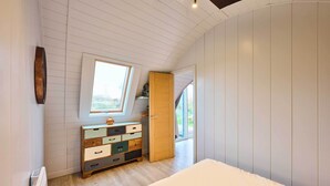Camera da letto con soffitto spiovente, una cassettiera in legno con numerosi cassetti, un letto e una finestra che fa entrare luce naturale.