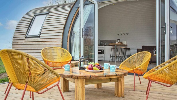 Una casa moderna con facciata curva, un pontile in legno e posti a sedere all'aperto.