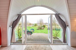 A view through a glass door with curtains, leading to an outdoor area with chairs and greenery. - Host & Stay | Secret Garden (Beccles)