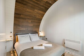 A modern bedroom with a curved ceiling, a bed with white linens, and a built-in heater.