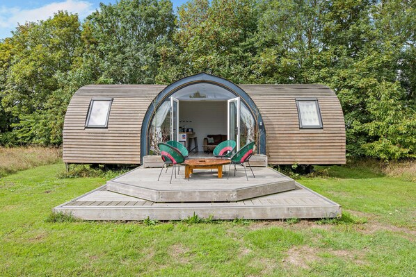 Una casa móvil con la parte delantera abierta, un patio con mesa y sillas, y una zona ajardinada alrededor.