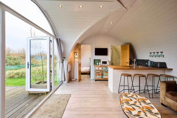 A modern kitchen with a bar area, a dining table, and a large window. - Host & Stay | Secret Garden (Beccles)