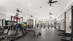 Uma academia com diversos equipamentos de exercício, ventiladores de teto e grandes janelas.