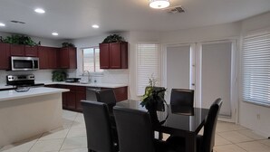 A modern kitchen with a dining area, featuring a central island, dark chairs, and recessed ceiling lights. - La Rosa Phoenix (Phoenix)