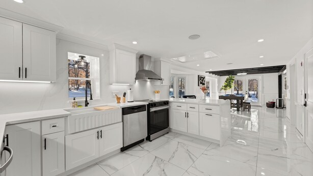 Una cocina moderna con armarios blancos, una isla central y vistas a un paisaje nevado a través de una ventana.