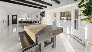 Una cocina moderna con armarios blancos, una mesa de comedor de madera y vistas a un paisaje nevado a través de amplios ventanales.