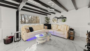 Una sala de estar moderna con un sofá modular, una mesa de centro de vidrio y un ventanal con vistas a árboles.