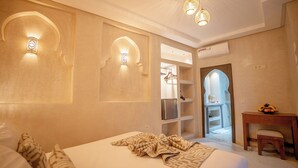 Une chambre d’hôtel avec un lit, un bureau et une armoire. On y trouve des appliques murales et un appareil de climatisation.