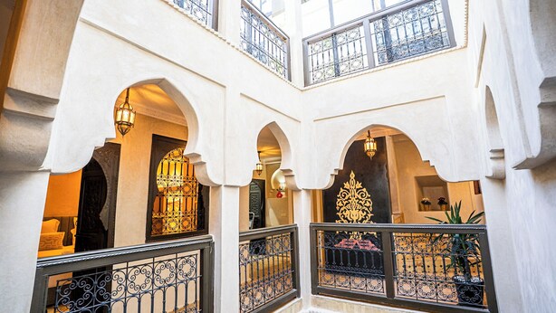 Un intérieur à plusieurs niveaux, agrémenté d’arcades, de rampes de fer forgé décorées et de lanternes suspendues.