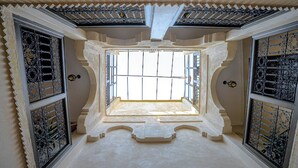 Une pièce dotée d’un plafond haut et richement décoré, ainsi que d’une grande fenêtre également ornée.
