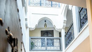 Une cour intérieure aménagée avec un canapé et des fauteuils, des plantes en pot et un escalier menant à un niveau supérieur.