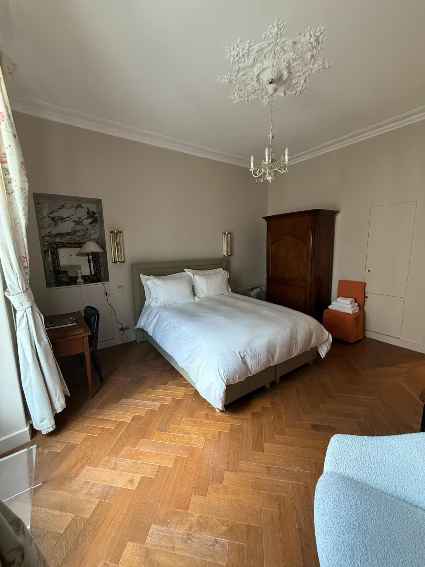 A bedroom with a large bed, a wooden wardrobe, a desk with a chair, and a chandelier.